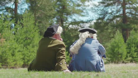 two gentlemen in 18th century attire sitting in a forest