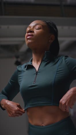 vertical video of determined female athlete zipping up tracksuit training in gym stretching and warming up preparing for sports event