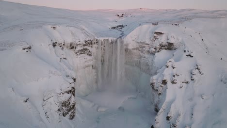 Luftaufnahme-über-Den-Skogafoss-Wasserfall,-In-Einer-Schneebedeckten-Winterlandschaft,-In-Island,-Bei-Sonnenuntergang