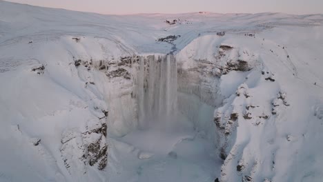 vista aérea sobre la cascada de skogafoss, en un paisaje invernal cubierto de nieve, en islandia, al atardecer
