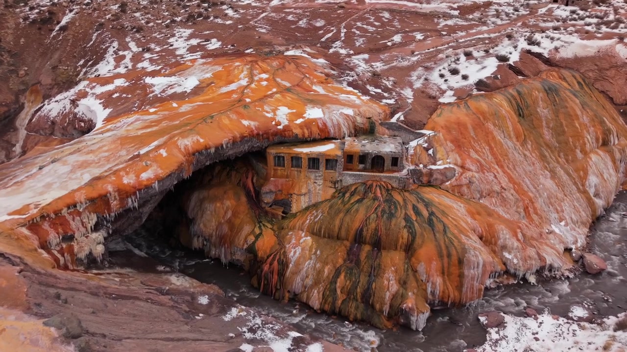 Ponte di roccia geotermico Puente del Inca a Mendoza, Argentina, che mostra formazioni ricche di minerali, erosione idrotermale e strutture montane abbandonate nel terreno innevato delle Ande, con avvicinamento in avanti tramite drone.