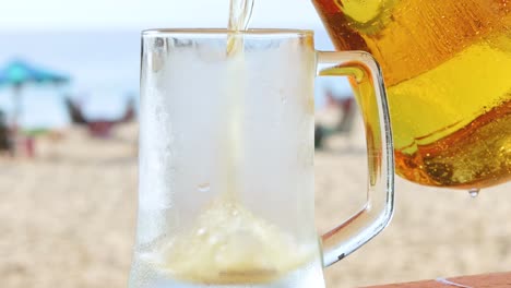 a refreshing drink is poured into a chilled glass on a sandy beach with umbrellas in the background.