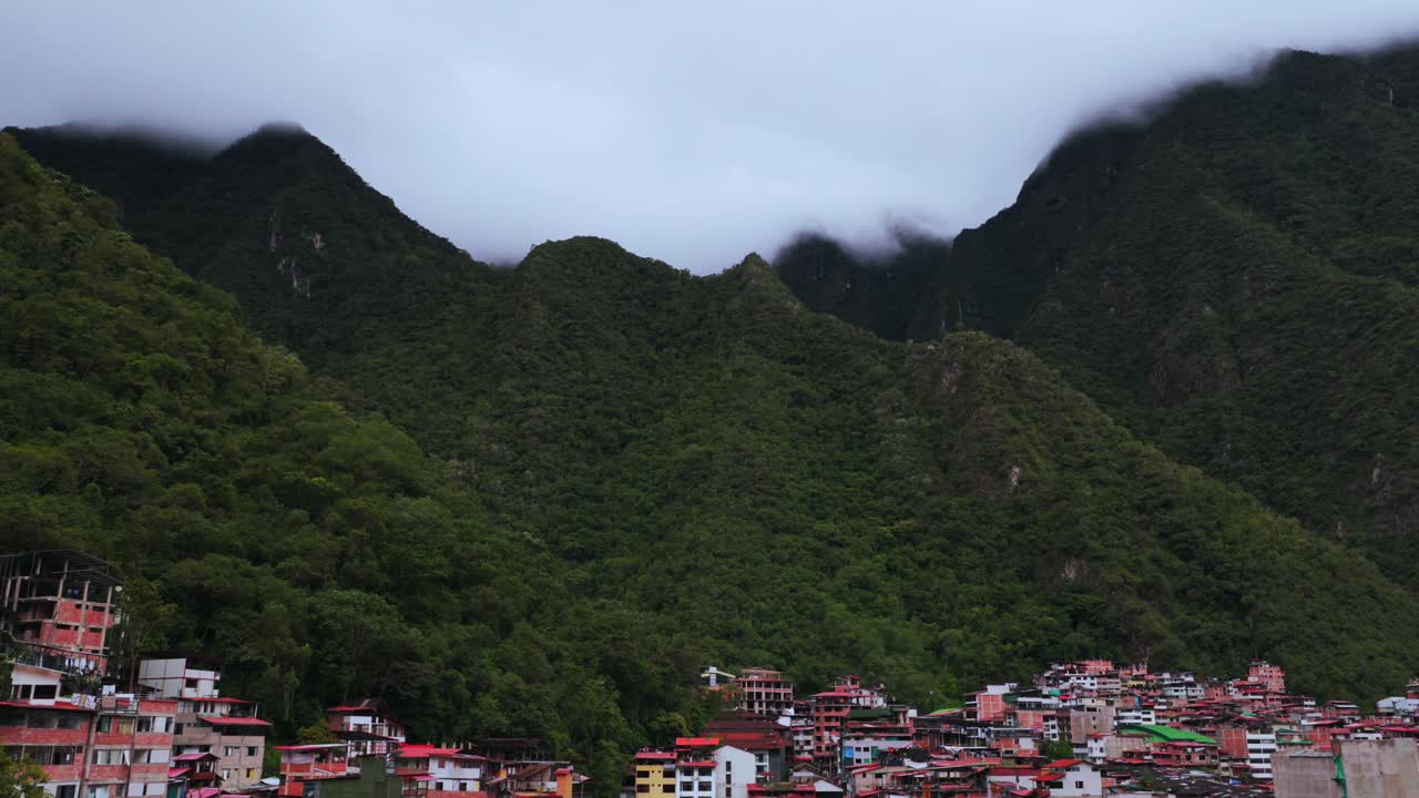 Aguas Calientes Machu Picchu town rainy season cloudy afternoon Peru aerial drone Peruvian Andes Mountains Urabumba river jungle lower highlands Inca trail citadel landscape buildings pan left
