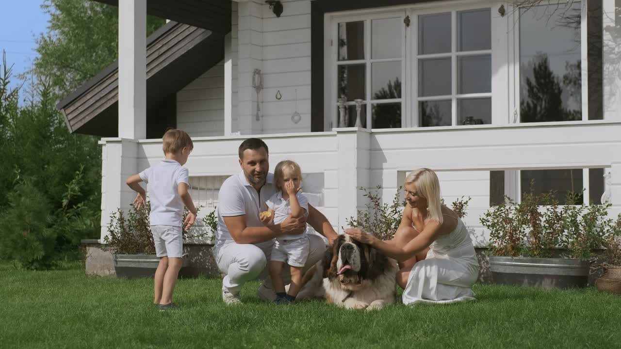 Una giovane famiglia di quattro persone e un cane che si divertono seduti vicino alla loro casa bianca.