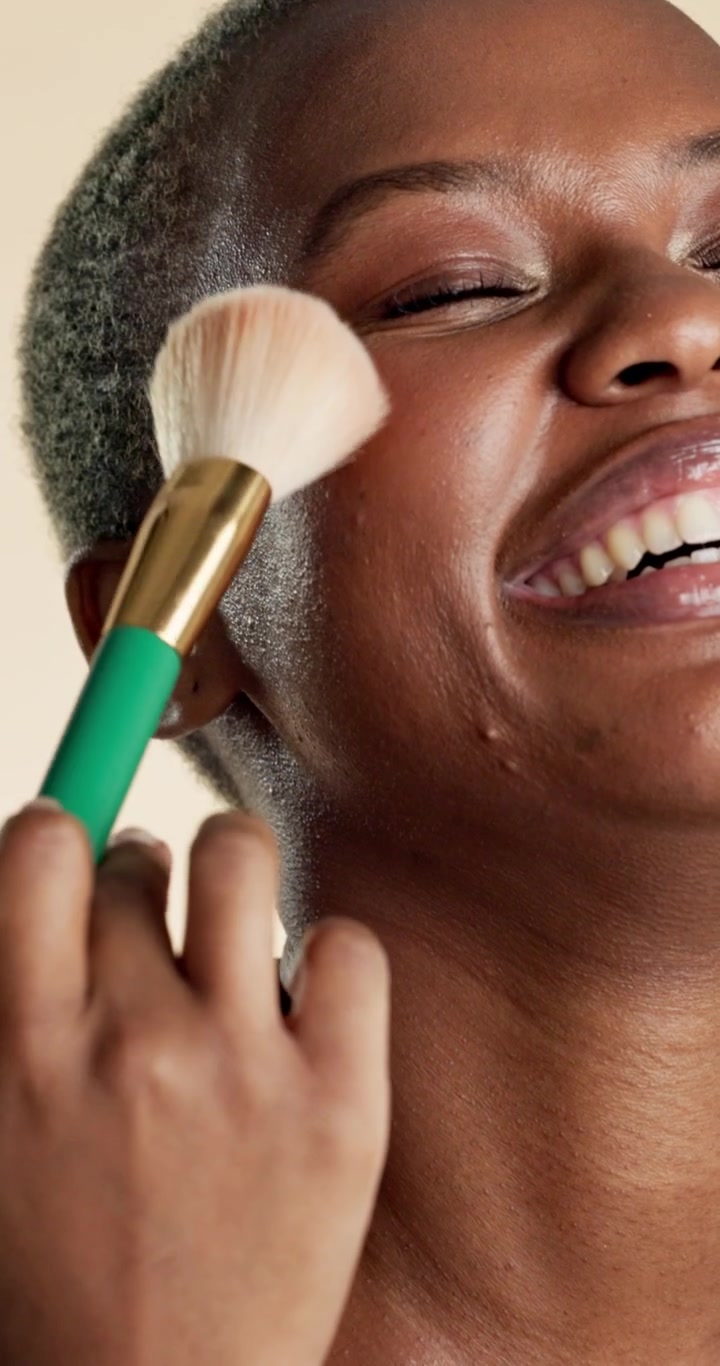 Smiling Young Woman Applying Makeup with Brush