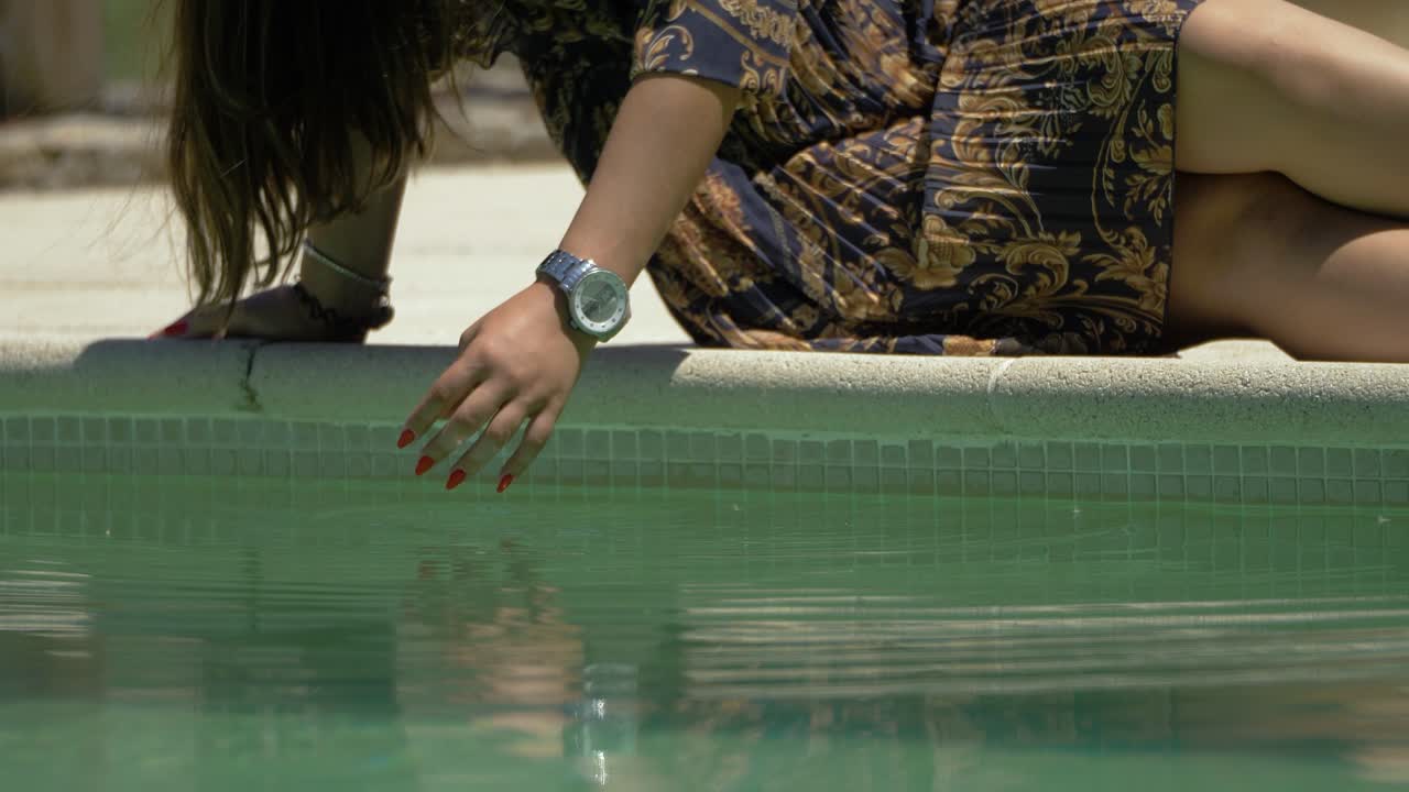 cámara lenta de mujer con vestido azul y dorado revolviendo tranquilamente en el agua de la piscina