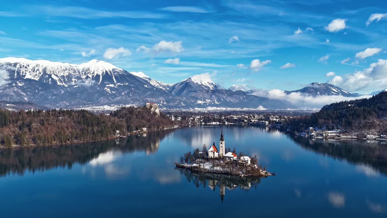 Il lago di Bled incornicia la chiesa innevata sull'isola e le Alpi nella nitida luce invernale, hyperlapse con drone in avanti
