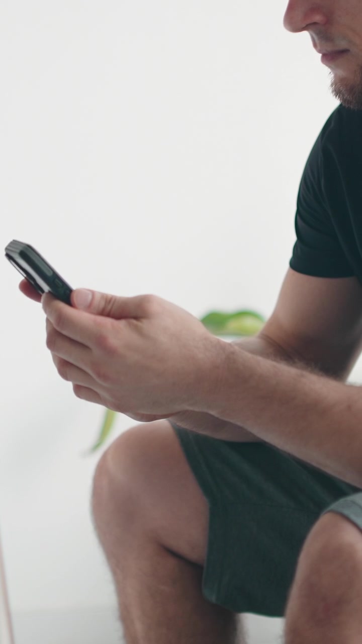 Giovane uomo seduto che usa lo smartphone in una stanza luminosa