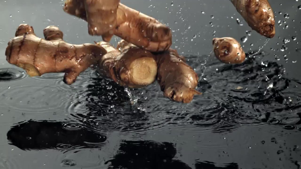 Radici di zenzero fresche che cadono nell'acqua con schizzi al rallentatore