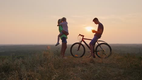 family on a walk standing at sunset with a bicycle