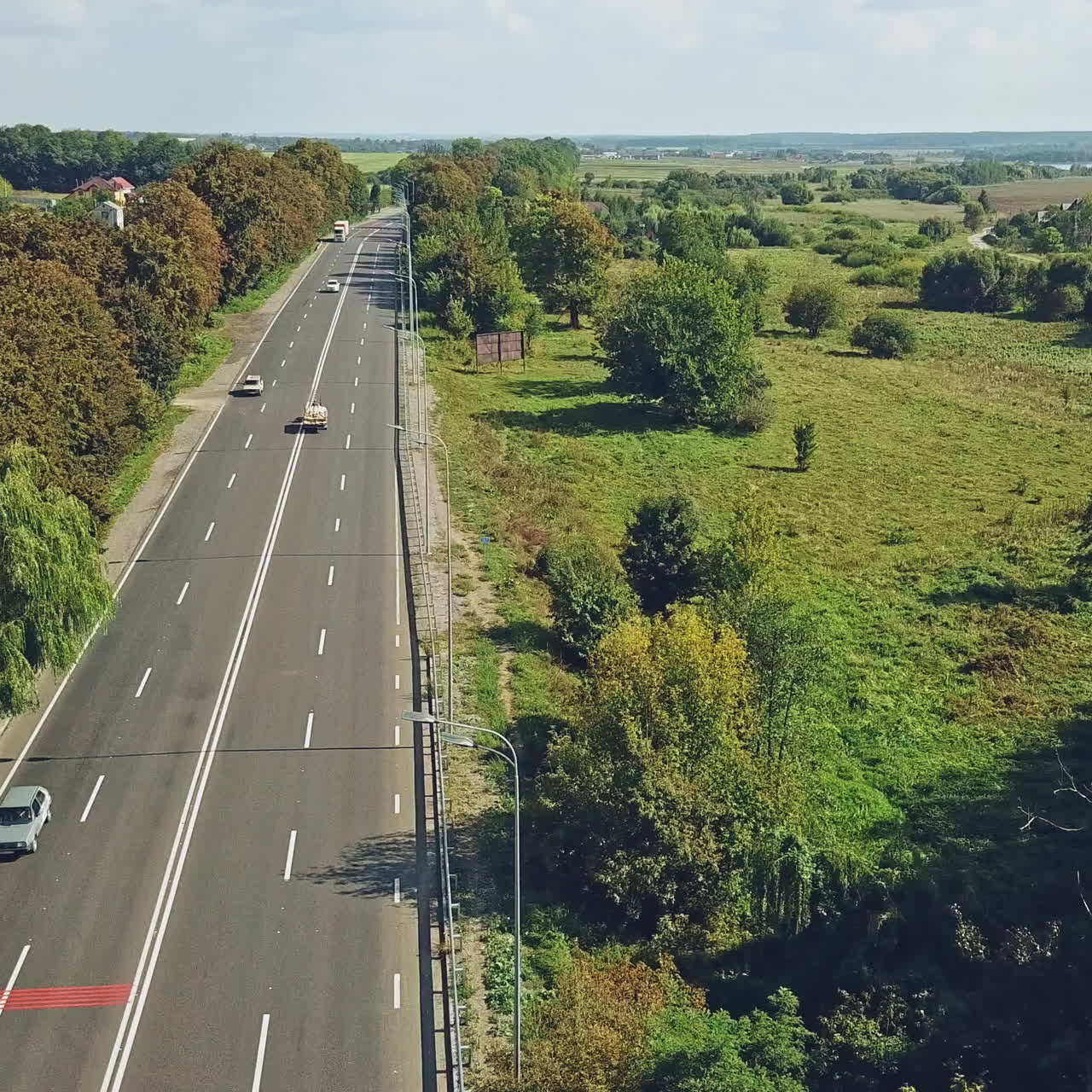 Aerial view of beautiful landscape of rural place with a wide road and cars on it in a sunny day. Various transport moving on the highway in different sides