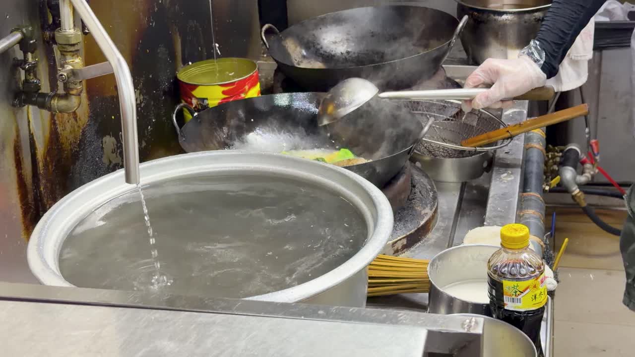 Ein Koch bereitet mit einem Wok und einem großen Kochtopf authentisches chinesisches Streetfood zu