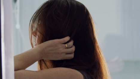 Side-view-of-middle-aged-brunette-woman-fixing-hair-in-bathroom-in-slow-motion