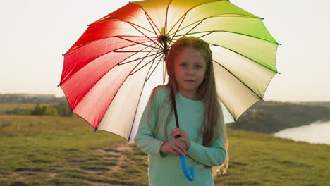 child rotates umbrella on riverbank at rain pretty little girl plays with large colorful parasol on