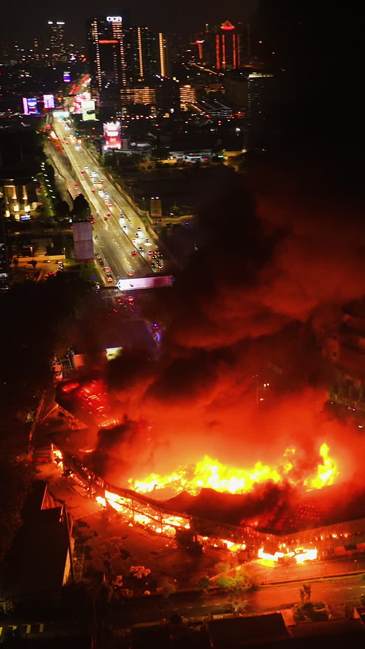 Vertical drone shot circling flames and smoke of a building fire, night in a city