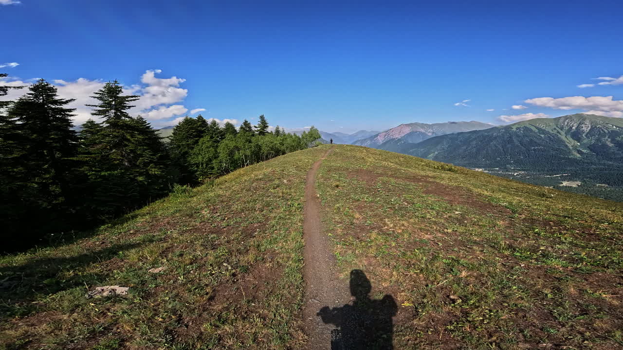 POV caminhando em trilha gramada de cume de montanha em direção a picos distantes