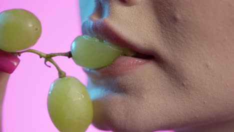 Mujer-Comiendo-Uvas-Blancas-En-Primer-Plano-De-La-Boca,-Esmalte-De-Uñas-Femenino-Y-Labios-De-Lápiz-Labial-Rojo-Sobre-Fondo-Rosa