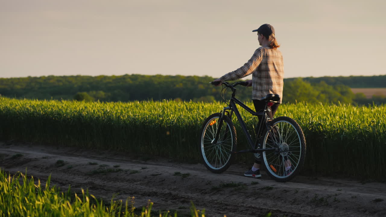 한 여성이 밀밭을 따라 자전거를 타고 여유롭게 산책을 즐깁니다.