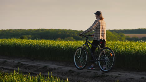 A-Woman-Leads-A-Bicycle-Along-The-Green-Fields-Of-Wheat-Enjoys-A-Leisurely-Walk