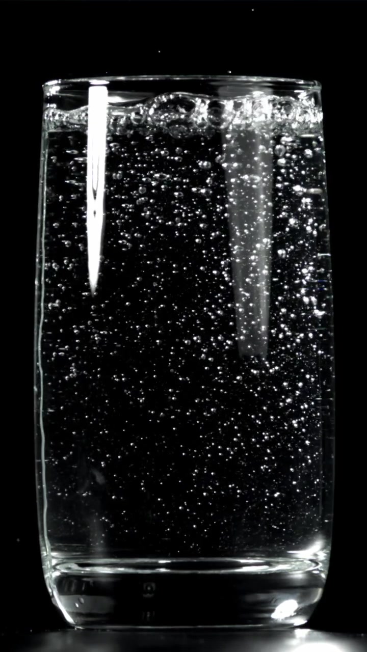 Acqua frizzante con bollicine che salgono in un bicchiere su sfondo nero