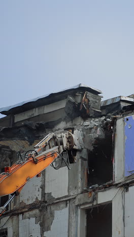 dismantling the upper floors of the multi-storey building. crushing the floors of the high house. excavator work in the deconstruction site. vertical video