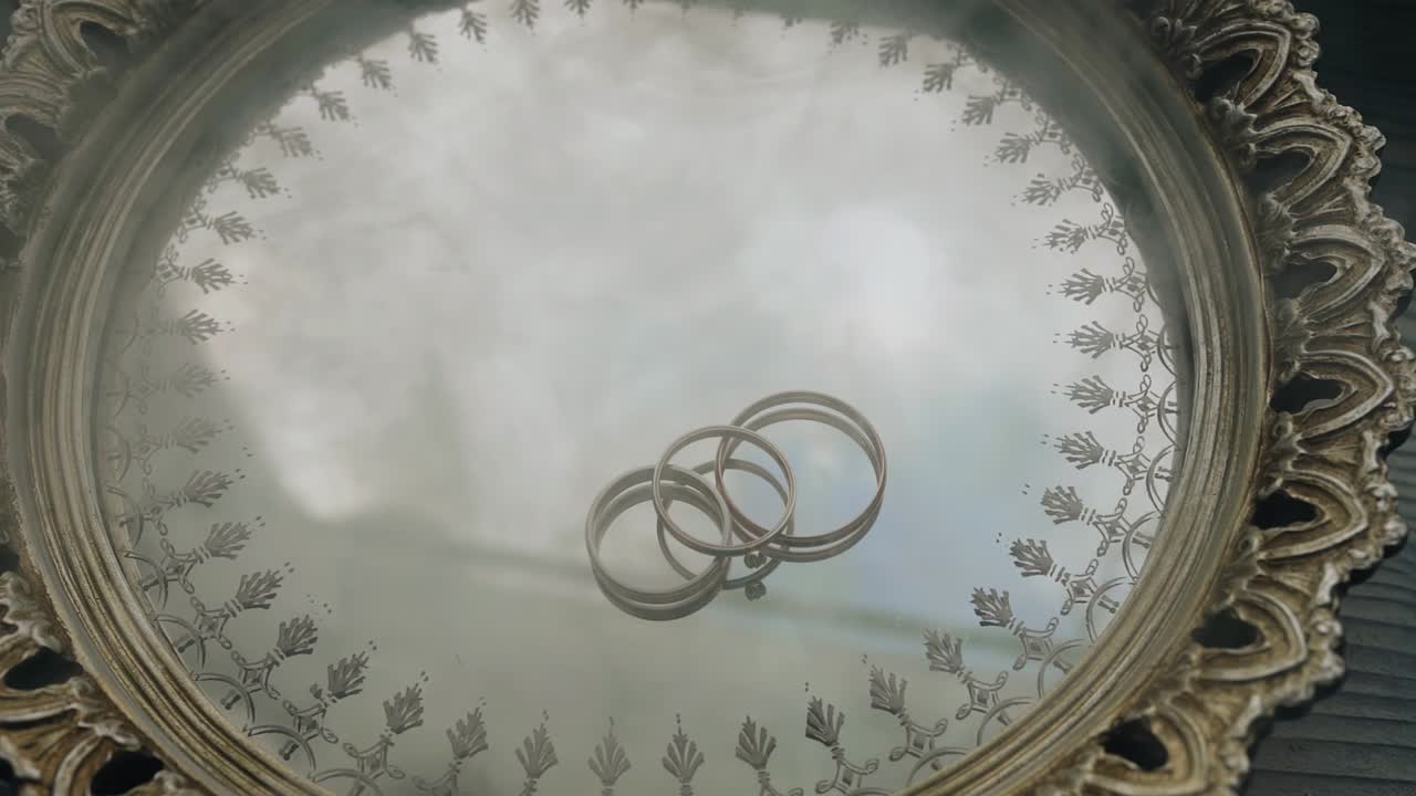 Three rings lie on a mirrored tray. Smoke appears from the side. Interesting composition