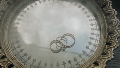 three rings lie on a mirrored tray. smoke appears from the side. interesting composition