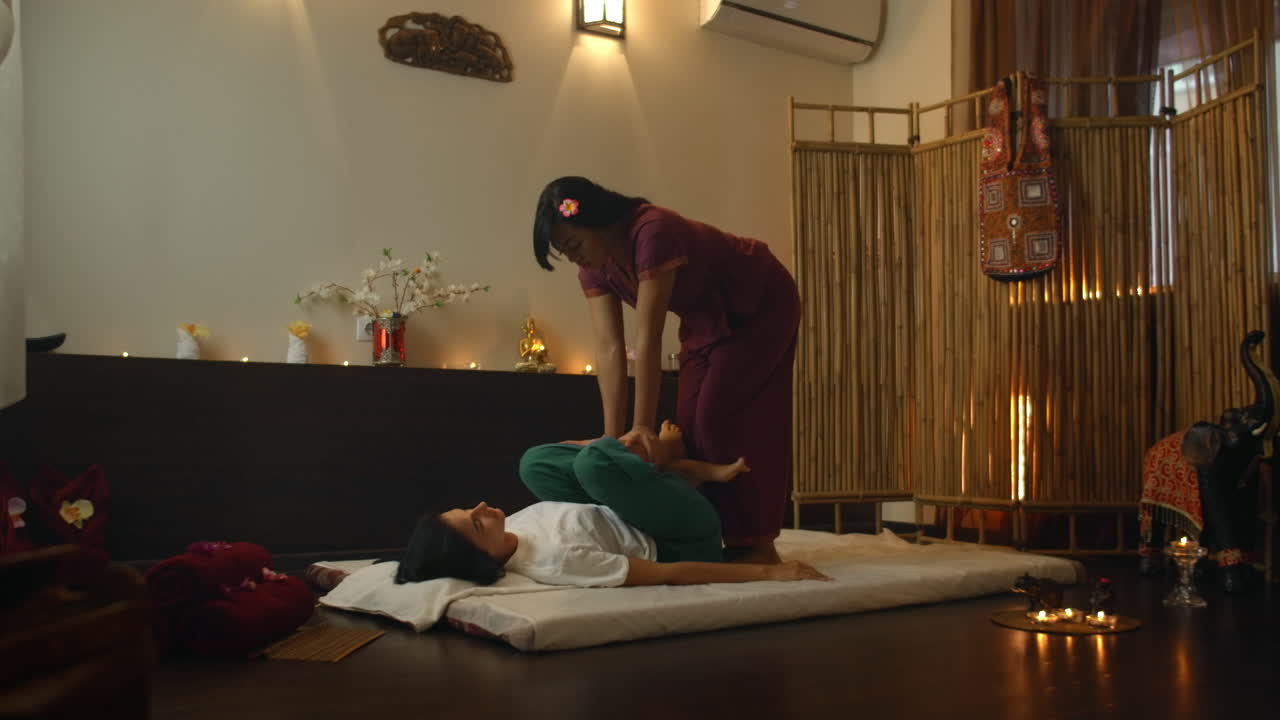 Asian Woman performs Traditional Thai Massage to beautiful European Woman. Rehabilitation and Treatment after Injuries with the help of Massage. Relax and Rest from massage of Legs Arms and Back. Therapeutic massage