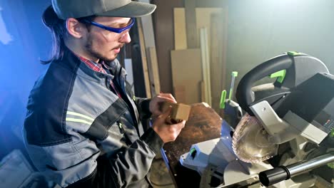 concentrated young bearded joiner in goggles and a cap checks the work piece