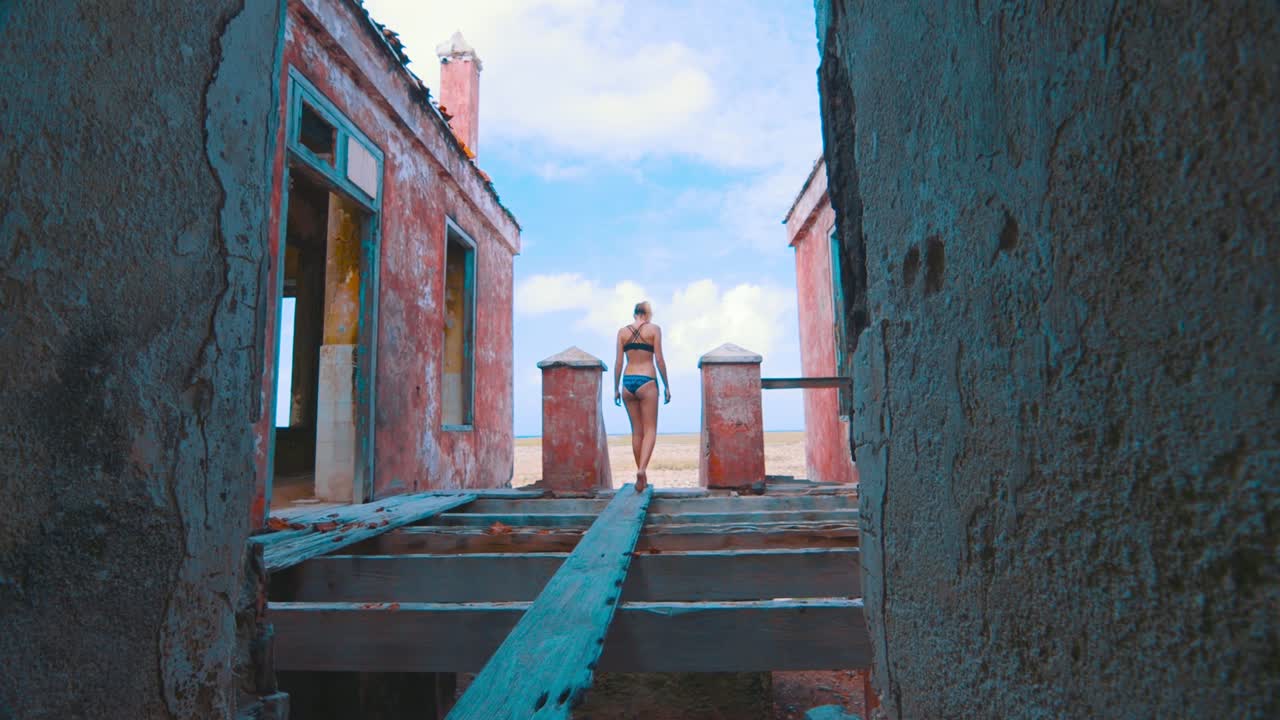 Girl in bikini walking over wooden plank in abandoned lighthouse
