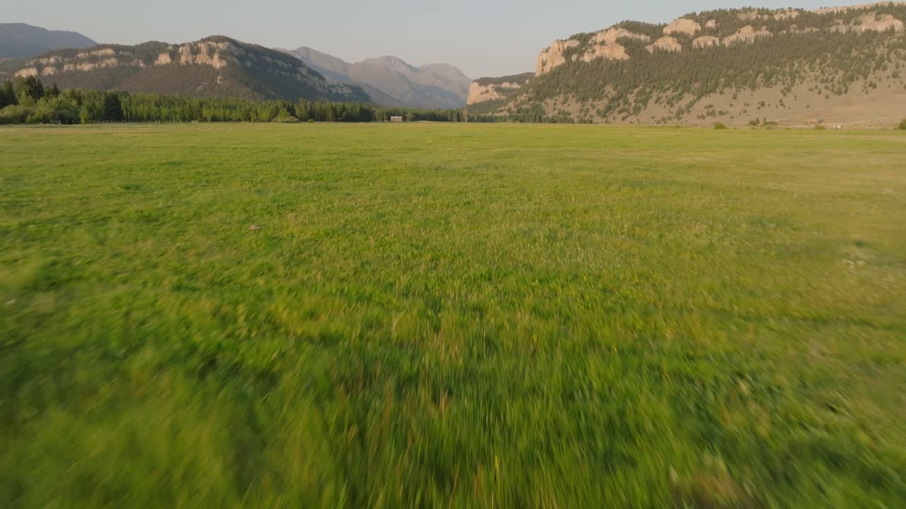 Aerial view over green grasslands as mountains emerge in the distance at sunset