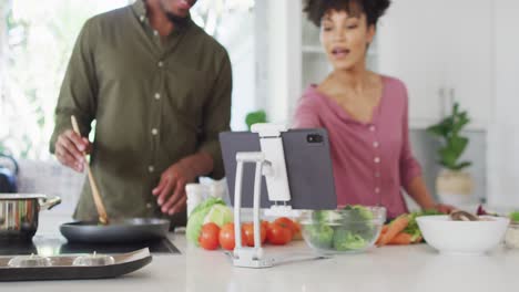 Happy-african-american-couple-cooking-and-using-tablet-in-kitchen