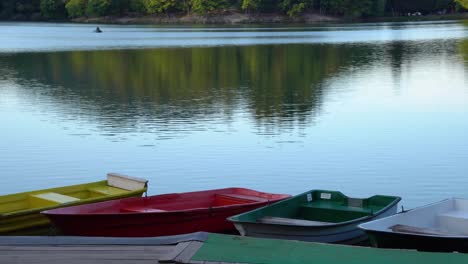 Colorful-boats-docking-on-the-side-of-the-calm-lake-on-summer-evening-sunset