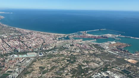 aerial side view of valencia city center recorded from an airplane cabin, with a view of harbor ant its north coast. bright summer day with an unclouded blue sky. 4k 60fps