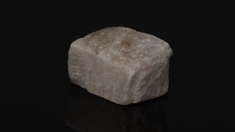 a beige mineral specimen rotates smoothly against a dark, reflective background, showcasing its texture and form.
