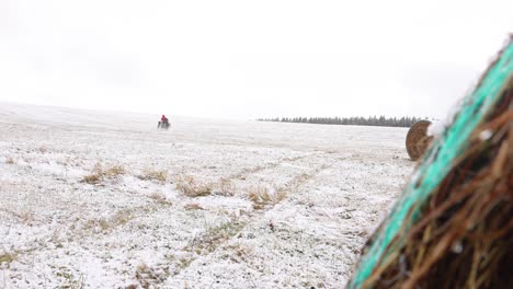 man riding a atv in a snowy field - snow covering grass on a farm 4x4 off-road drifting