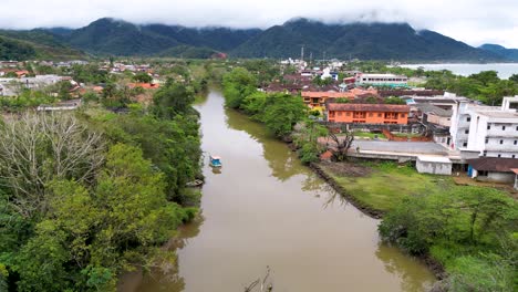 aerial view of a river in the middle of a village and mountains on background - ubatuba, brazil