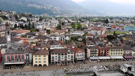 aerial flyover over the rooftops of ascona in ticino, switzerland towards the shores of lago maggiore, with a boat departing from the waterfront towards the lake with a view of the alps