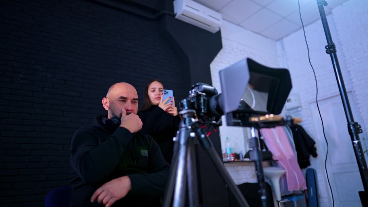 Työntekijät säätävät teleprompteria ja kameran asetuksia ammattistudiossa. Nainen ja mies asentamassa kamera- ja teleprompterilaitteistoa videokuvaukseen studioympäristössä.