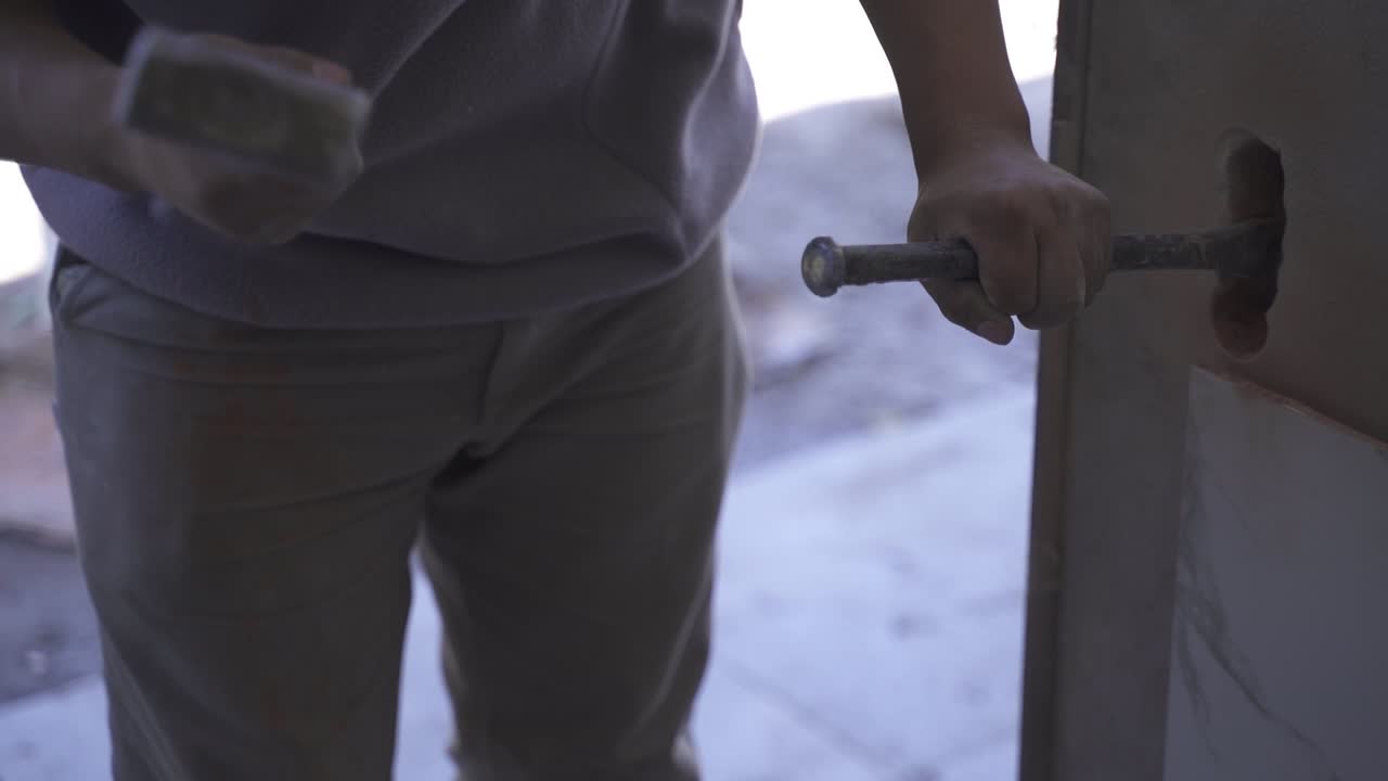 Close up shot of a worker making a hole in a wall with a hammer and chisel