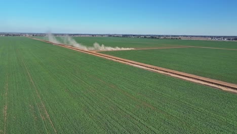 Wide-aerial-of-a-tractor-and-equipment-driving-along-a-dirt-road-on-a-farm