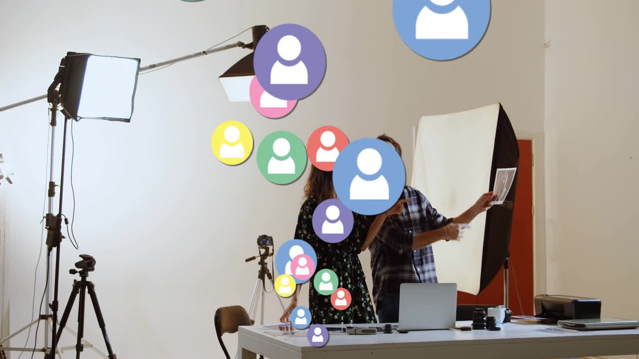 Dúo creativo discutiendo la composición, lo que hace que iconos de usuario coloridos asciendan y rodeen un escritorio de estudio