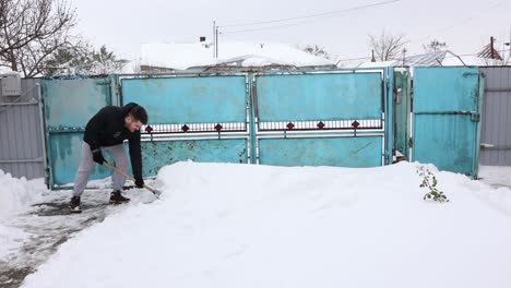 Hombre-Limpiando-Nieve-Con-Una-Pala-Cerca-De-La-Puerta-Oxidada---Ancha