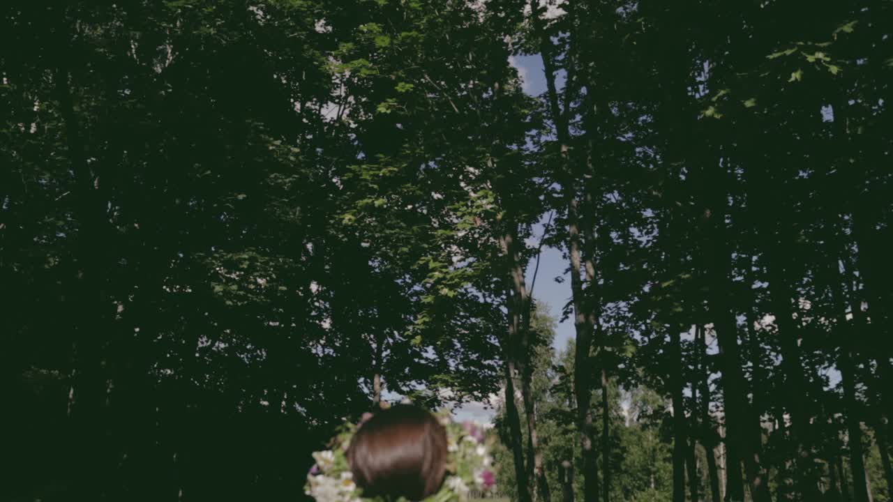 여름 최고점을 준비할 준비가 된 꽃 왕관을 가진 여성, 색상 등급, 카메라가 나무 꼭대기와 하늘까지 기울어지고 슬로우 모션