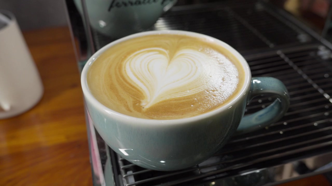 Primer plano de barista, arte latte de corazón en taza de café de cerámica, en toma orbital, detalles de la bebida.