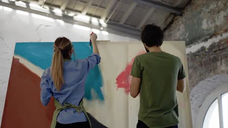 young couple paints on canvas drawing picture in art studio and kissing