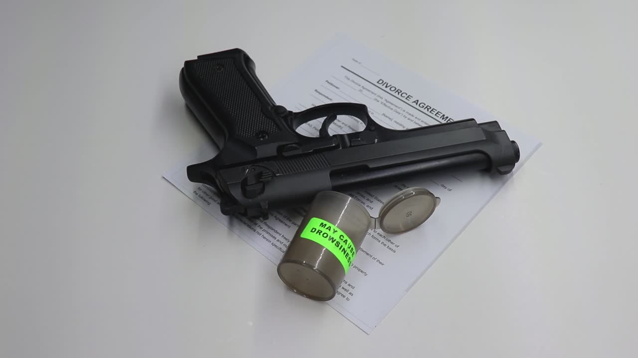 persona tomando un puñado de pastillas para dormir luego recoge un arma de fuego negra con papeles de divorcio dejados visibles en la mesa