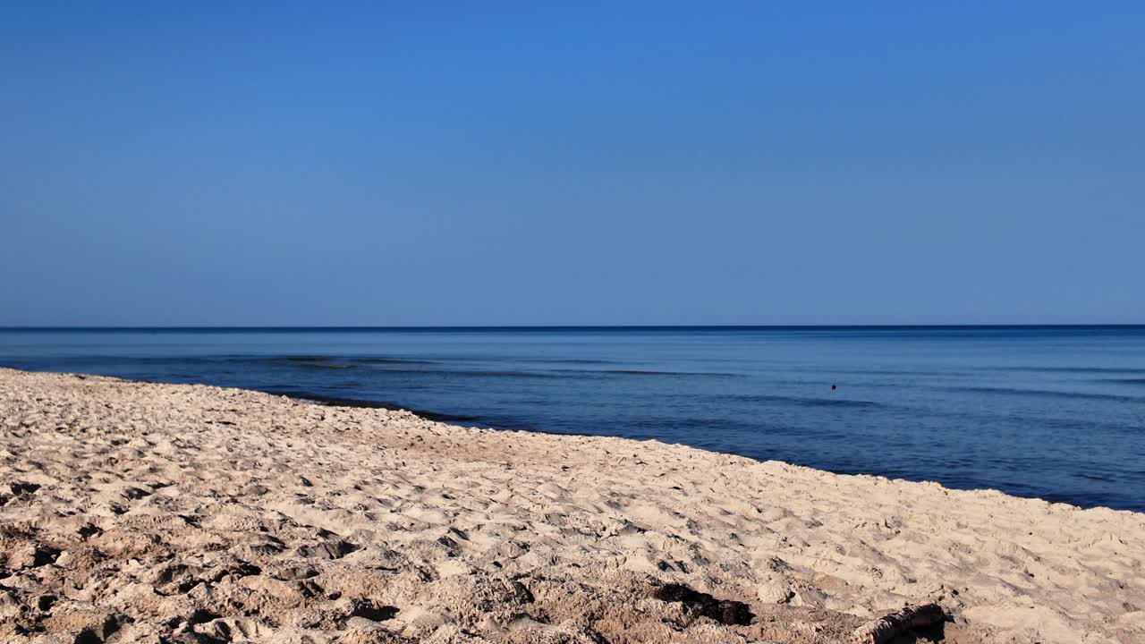 Peaceful sandy beach with calm blue sea and clear sky, creating a serene and tranquil coastal landscape perfect for relaxation or travel themes