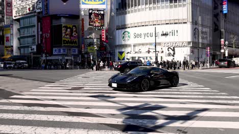 black sports car driving across a busy urban crosswalk