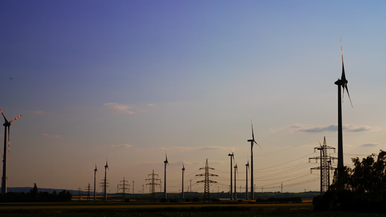 Beautiful sky at sunset with silhouettes of windmills and electric towers. Energy production and transmission concept.